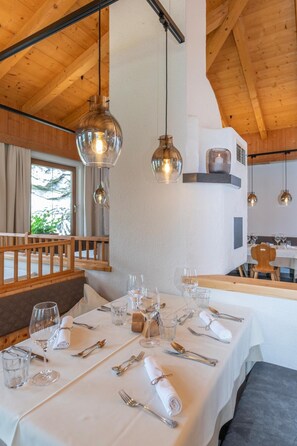 A dining area with tables set for a meal, wooden beams on the ceiling, and hanging pendant lights.