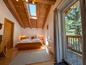A bedroom with a wooden ceiling, a large bed, bedside lamps, a window, and a view of a balcony.