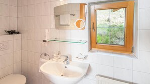 A bathroom with a toilet, sink, mirror, and window.
