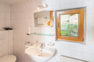 A bathroom with a toilet, sink, mirror, and window.