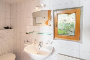 A bathroom with a toilet, sink, mirror, and window.