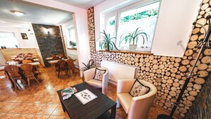 A dining area with wooden chairs and a table, a seating area with a sofa and armchairs, and a wall decorated with wooden logs. - Hostel & Apartments u Florka 2 (Zakopane)