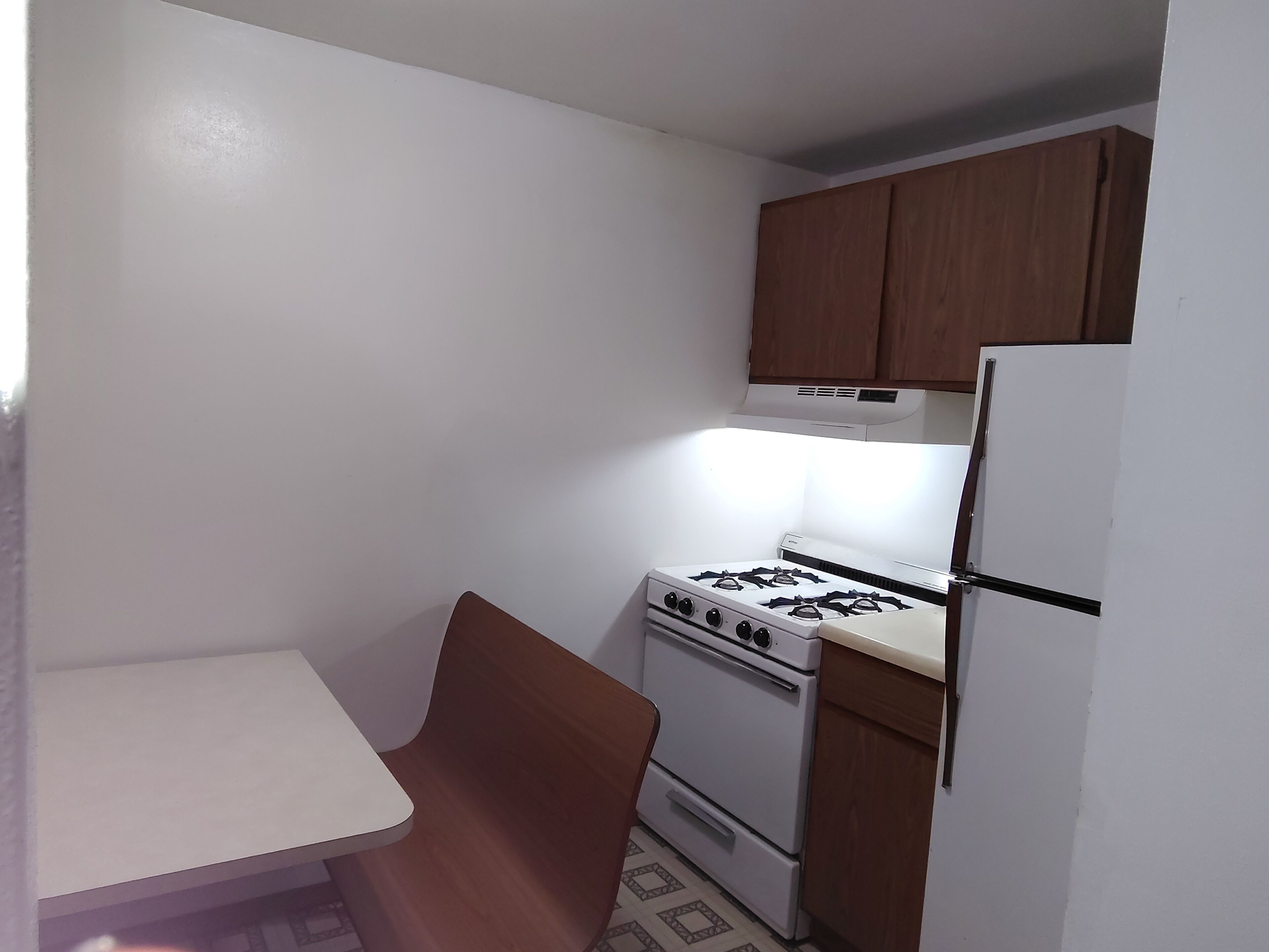 A small kitchen with a white stove, a refrigerator, and wooden cabinets.
