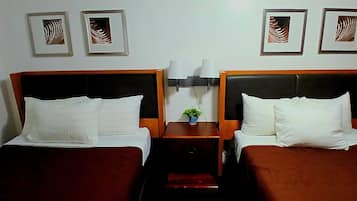 Quarto de hotel com duas camas, mesa de cabeceira com abajur e obras de arte emolduradas na parede.