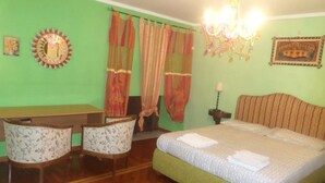Una habitación con cama, dos sillones, un escritorio, una araña y cortinas.