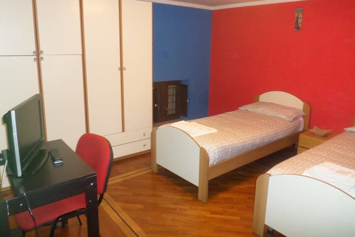 Una habitación con dos camas individuales, un escritorio con silla, un armario y un pequeño mueble.