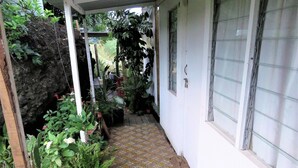 Een overdekte veranda met een betegelde vloer, plantenpotten en een witte muur met een raam.