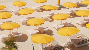 A beach with rows of yellow umbrellas and white lounge chairs. - Palm Heights (Seven Mile Beach)
