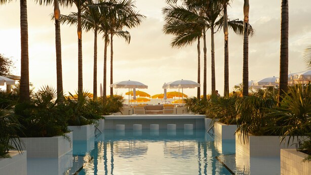 A swimming pool with a view of palm trees and umbrellas. - Palm Heights (Seven Mile Beach)