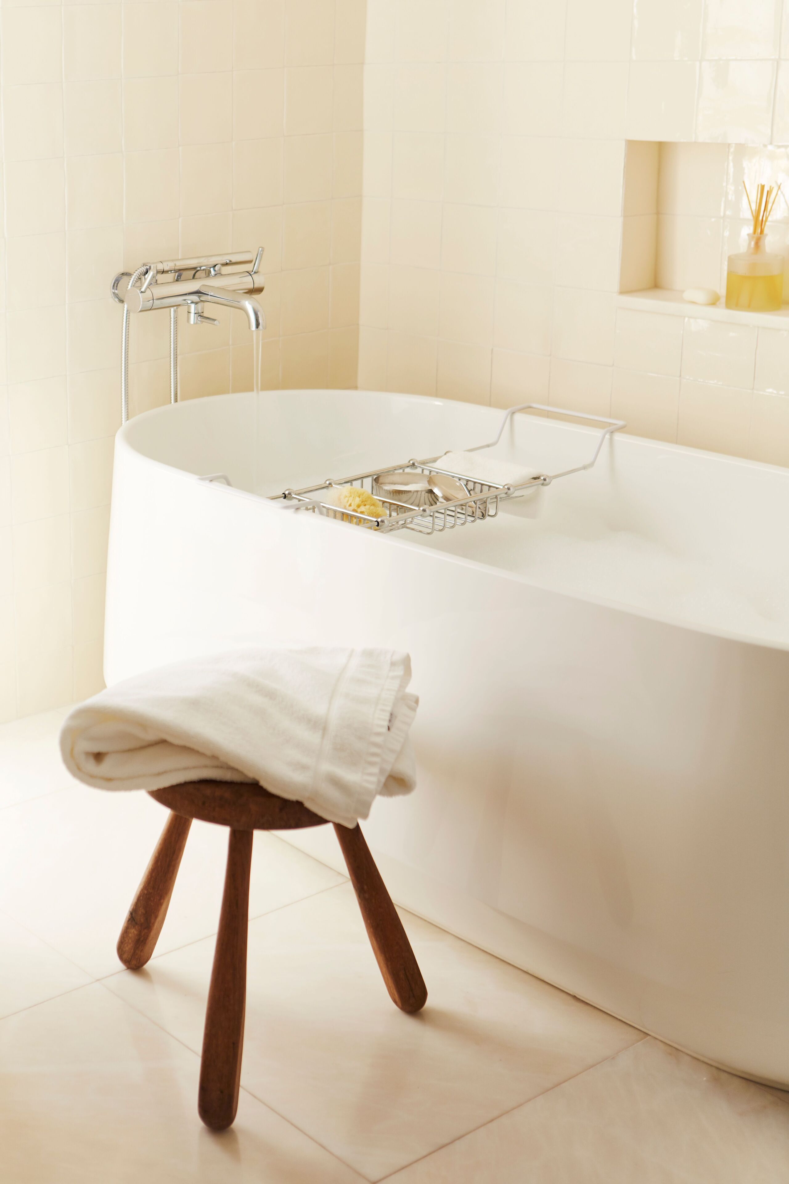 Un baño moderno con una bañera independiente, un taburete de madera con una toalla y un pequeño estante con artículos de aseo.