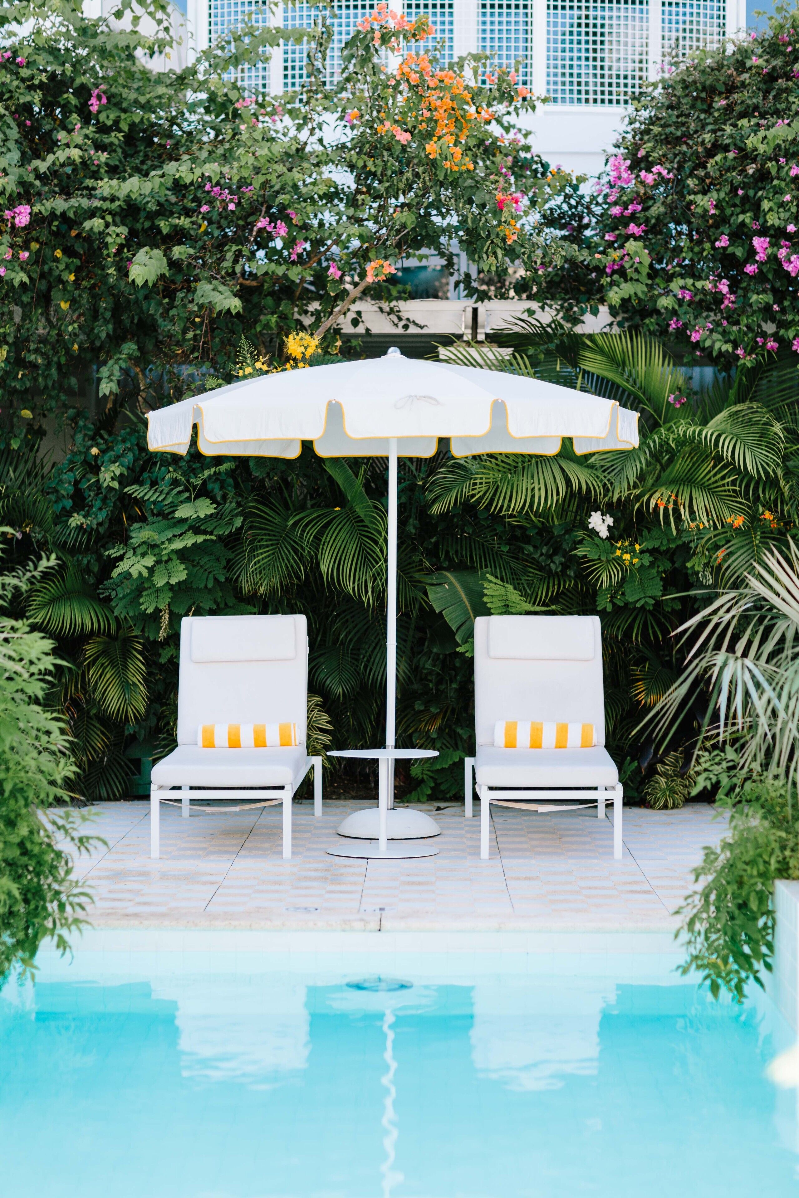 A poolside area with two white lounge chairs and a white umbrella.