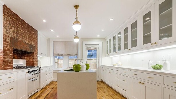 Une cuisine moderne avec des meubles blancs, un îlot central, un four à briques et un plancher en bois.
