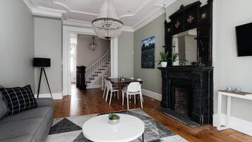 A living room with a fireplace, a chandelier, and a dining area with chairs and a table.