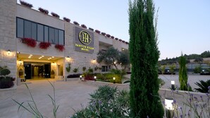A hotel entrance with a stone facade, a sign reading "Tantuk Hills Hotel," and a well-lit outdoor area with plants and pathways. - Tantur Hills Hotel - Jerusalem (Jerusalem)