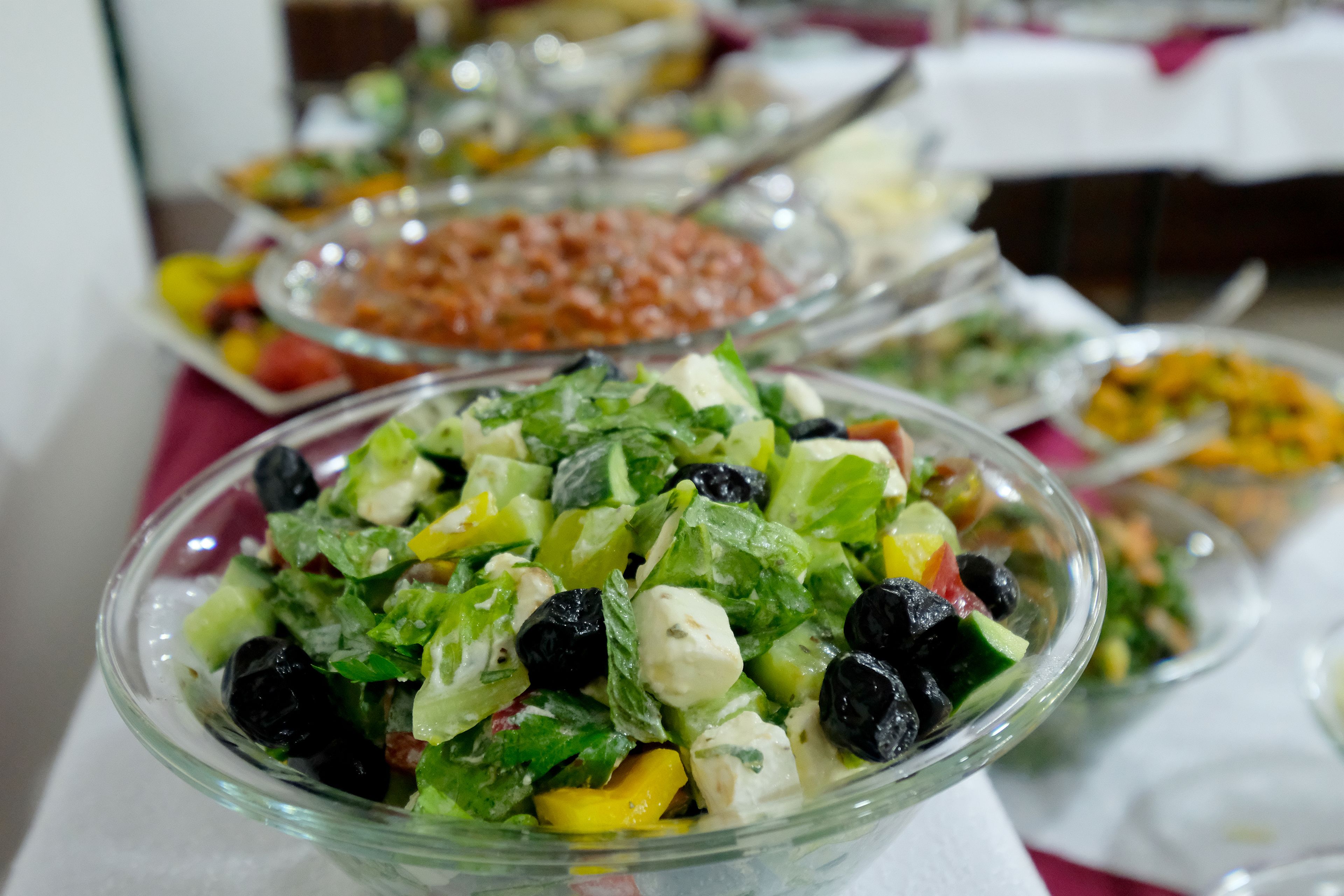 Ein reichhaltiges Buffet mit verschiedenen Speisen, darunter ein Salat mit Blattsalaten, schwarzen Oliven und Käse.