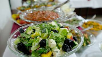 Ein reichhaltiges Buffet mit verschiedenen Speisen, darunter ein Salat mit Blattsalaten, schwarzen Oliven und Käse.
