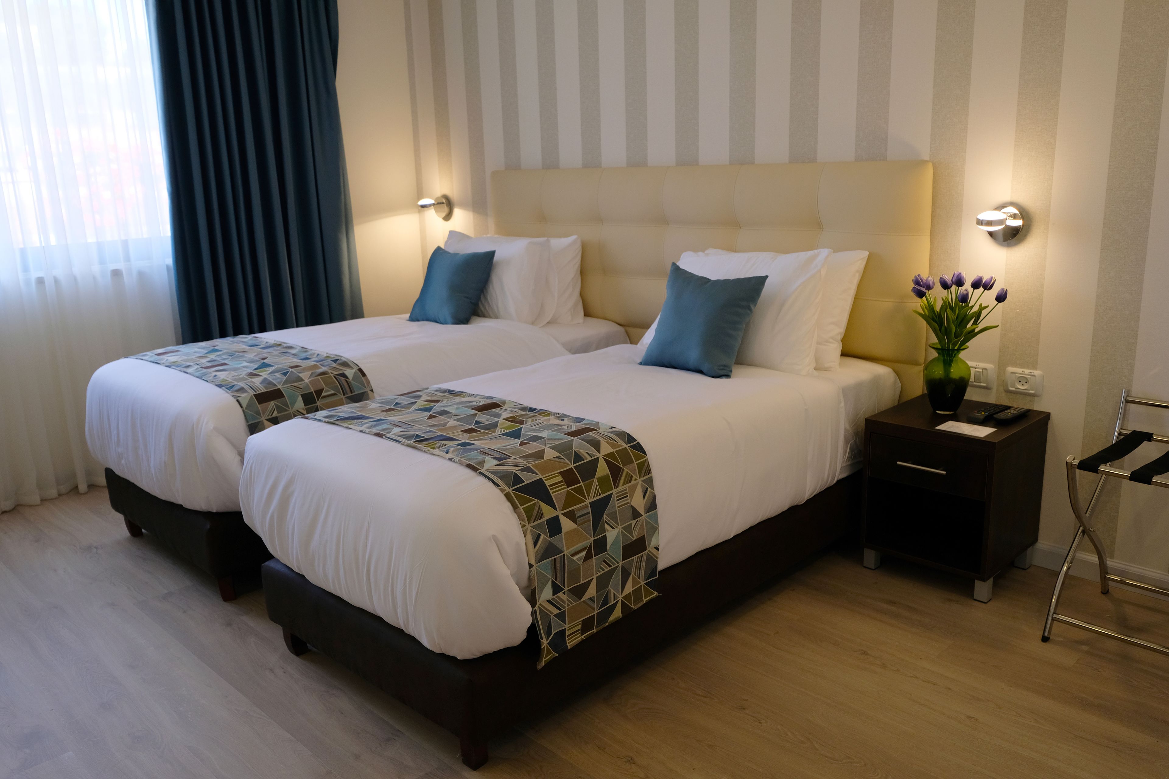 Una habitación de hotel con dos camas, una mesita de noche, una lámpara y un jarrón con flores.