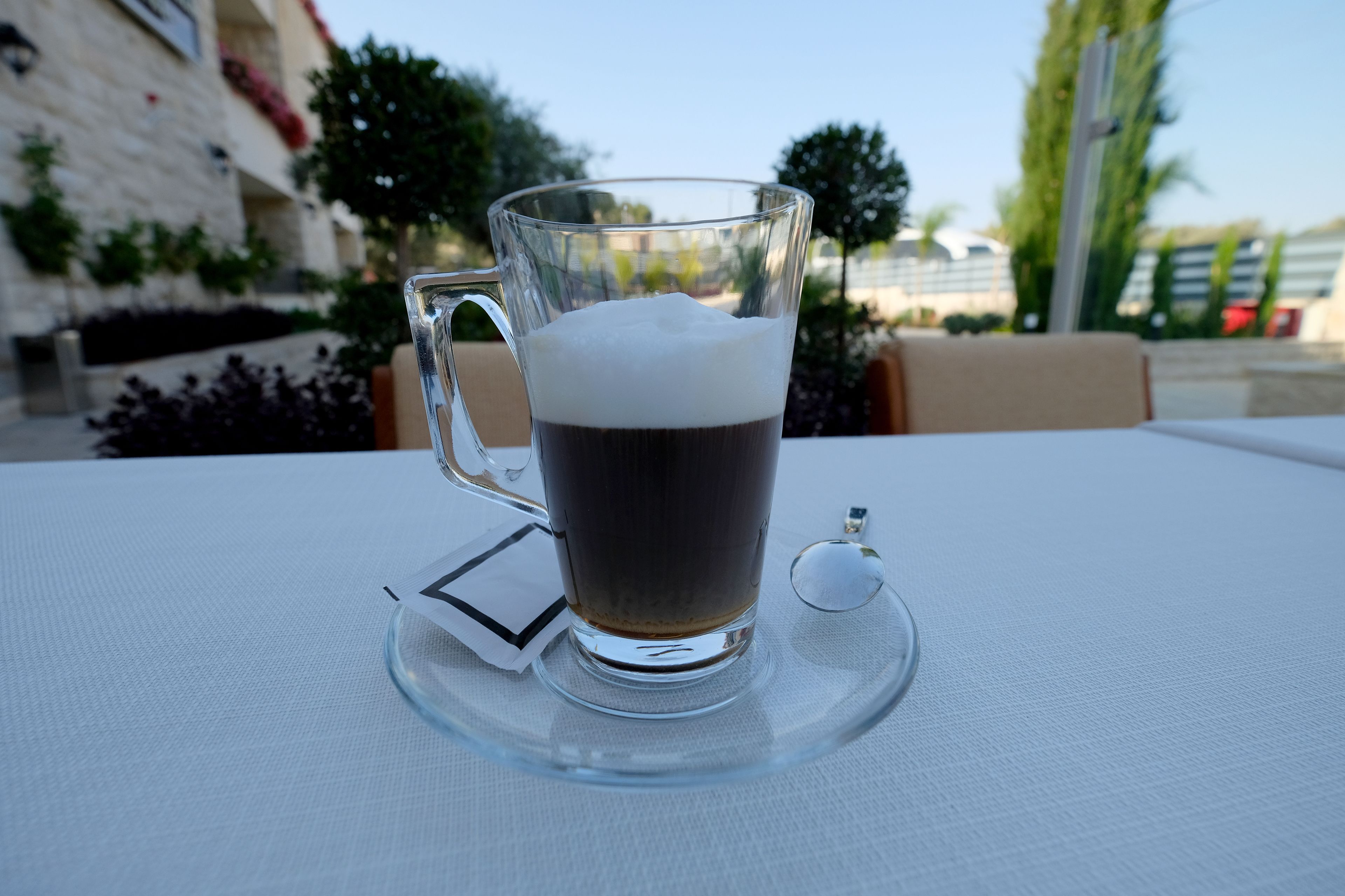 A clear glass mug with a handle on a white tablecloth, placed on a clear coaster.