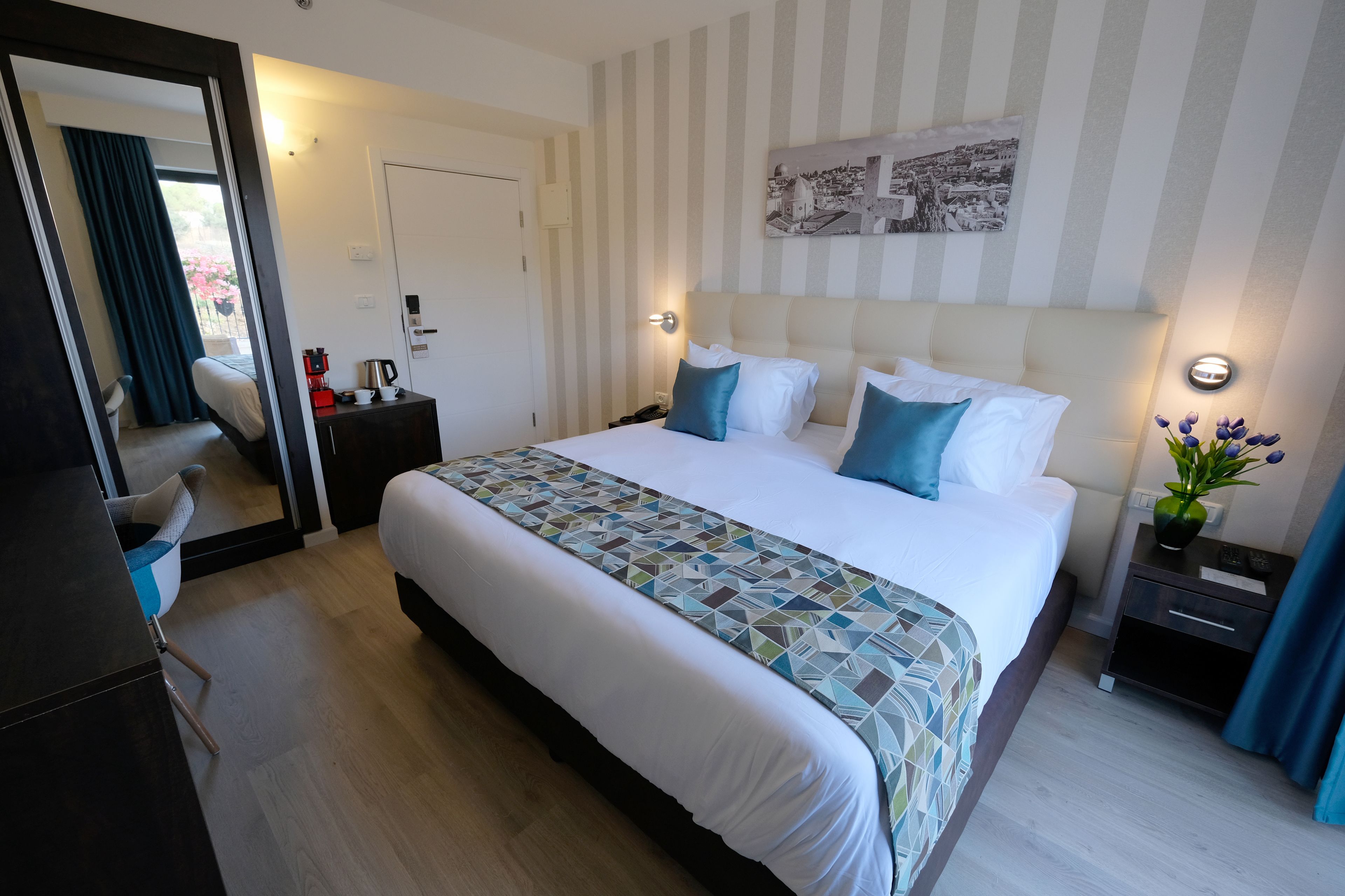 A hotel room with a large bed, a bedside table with a lamp, a nightstand, a chair, and a view of the outdoors.