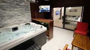 A modern bathroom with a large bathtub, a wooden vanity, a television, and a red chair. - Tantur Hills Hotel - Jerusalem (Jerusalem)