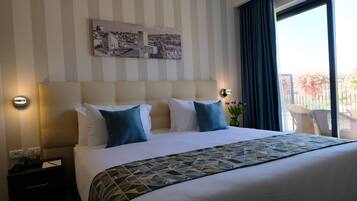Een hotelkamer met een groot bed, een hoofdeinde met twee nachtkastjes, een wanddecoratie en uitzicht op een balkon met bloemen.