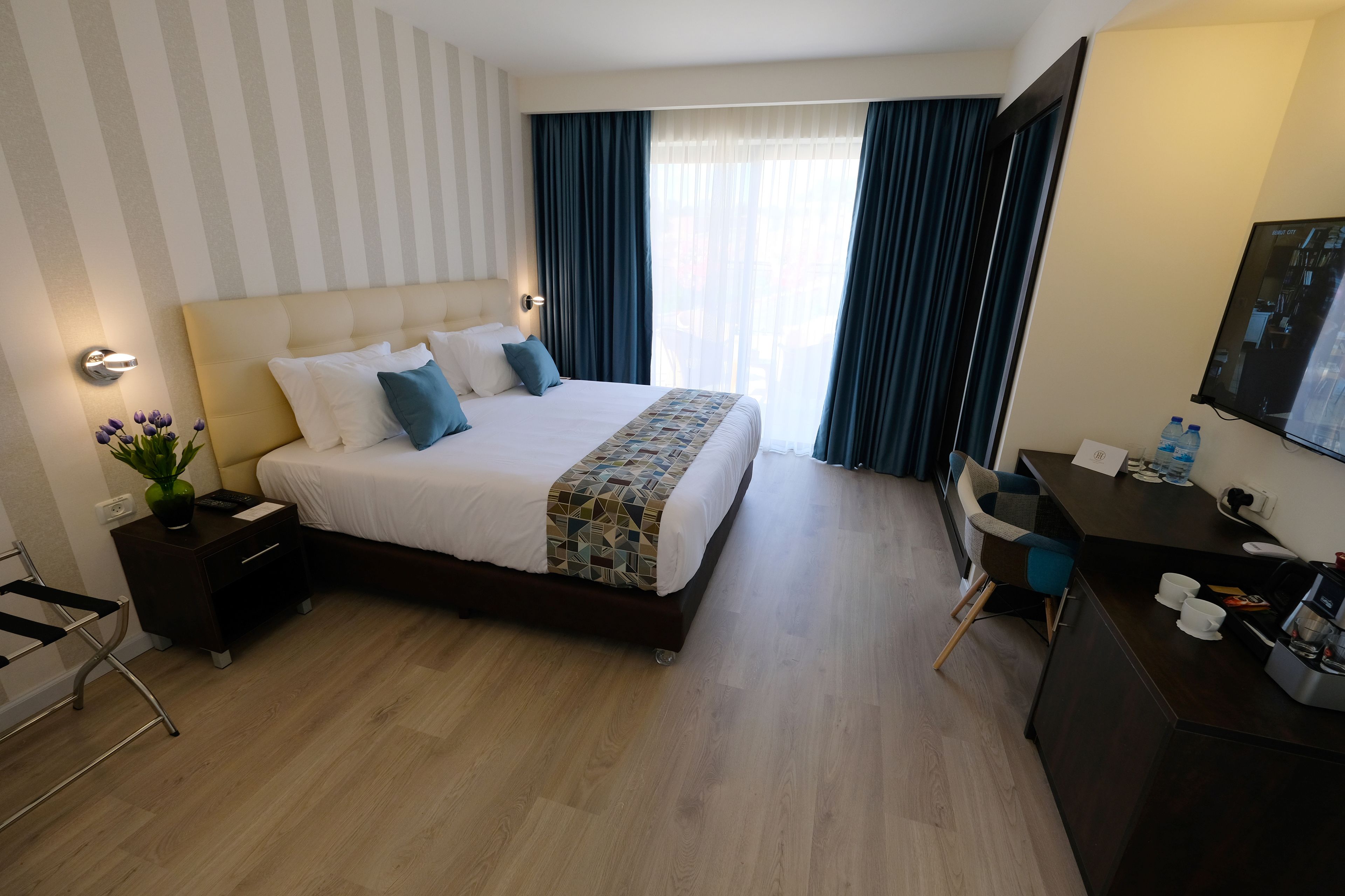 Ein Hotelzimmer mit einem großen Bett, einem Schreibtisch, einem Sessel, einem Fernseher und einem Fenster mit Vorhängen.