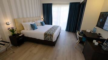 Ein Hotelzimmer mit einem großen Bett, einem Schreibtisch, einem Sessel, einem Fernseher und einem Fenster mit Vorhängen.
