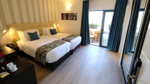 A hotel room with a large bed, a desk with a lamp, and a view of the outdoors through a sliding door. - Tantur Hills Hotel - Jerusalem (Jerusalem)