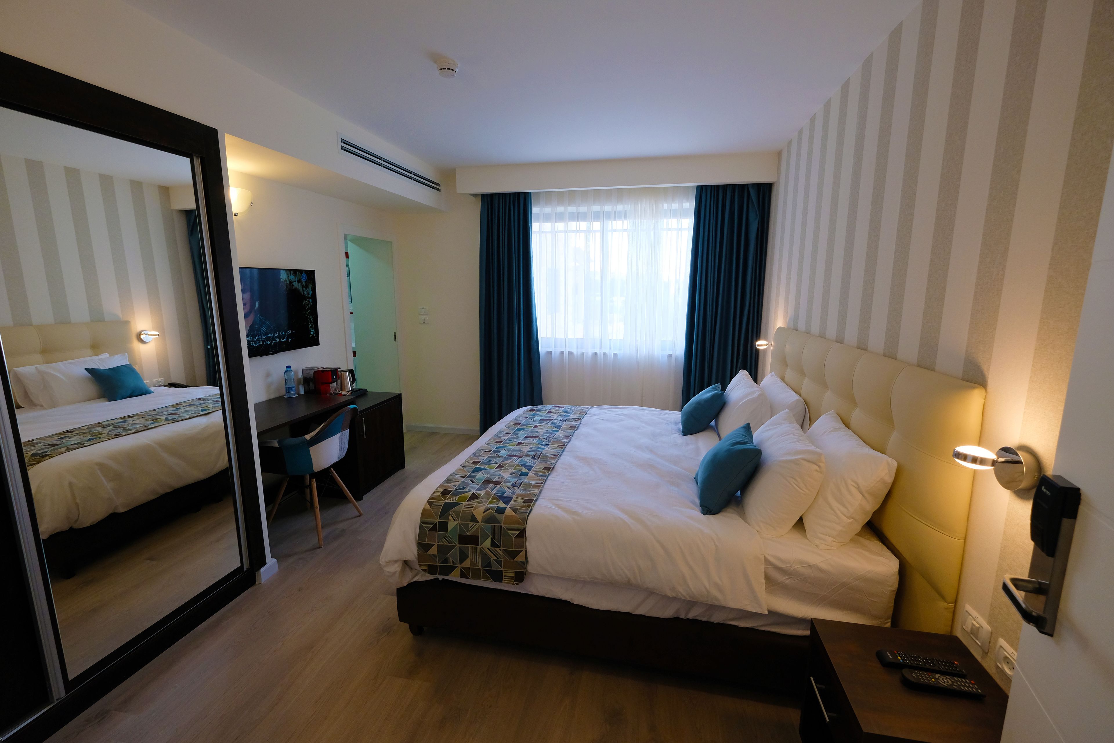 A hotel room with a large bed, a desk, a mirror, and a TV.