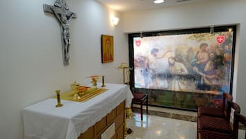 Features a crucifix, a religious painting, and a wooden altar in a peaceful space with a view of greenery.