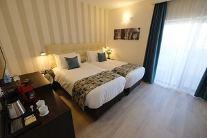 Habitación de hotel con dos camas, un rincón para café y vistas a la ciudad a través de cortinas traslúcidas.