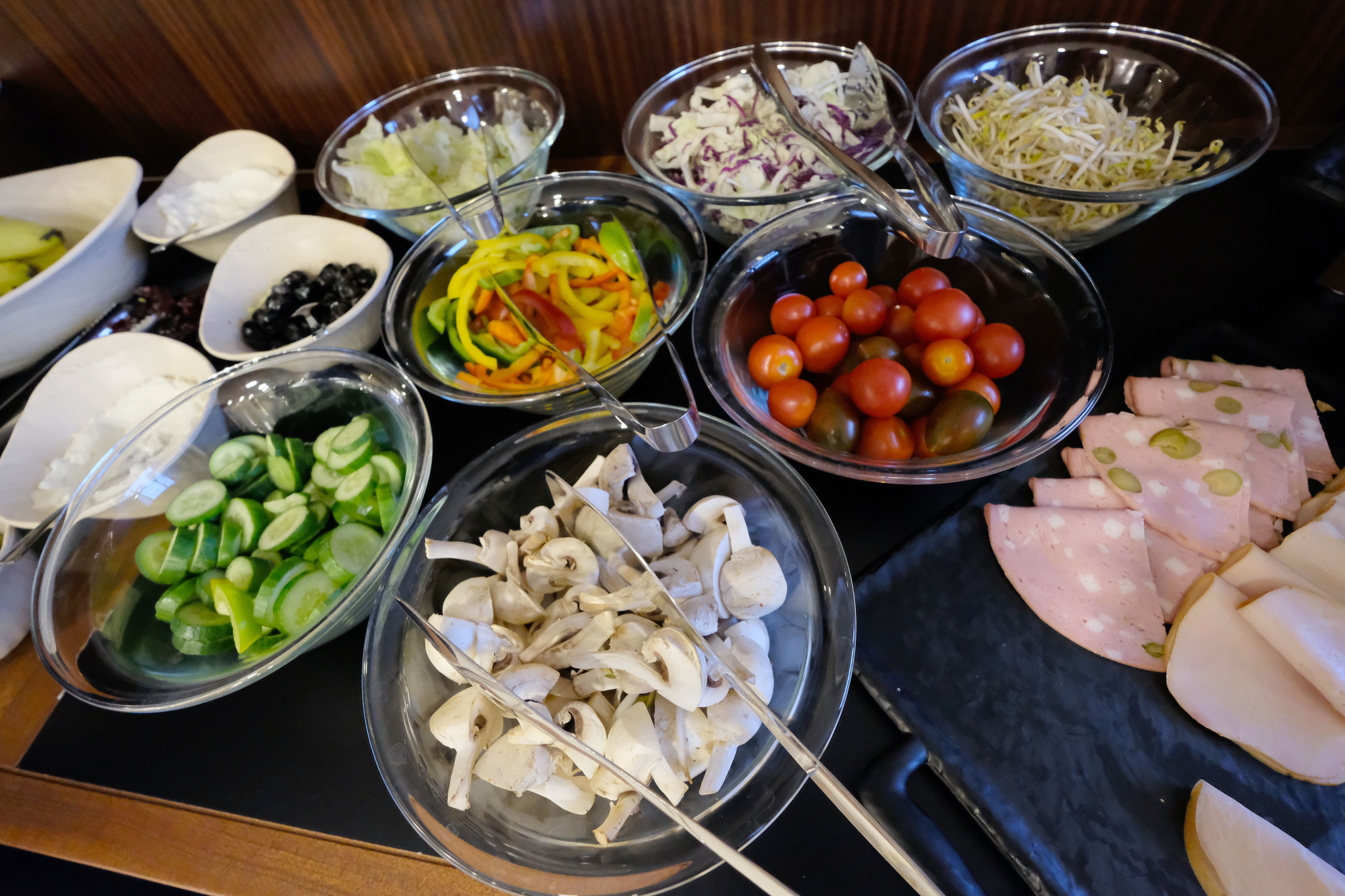 Una mesa con diversos alimentos, como rodajas de pepino, champiñones, tomates y carne cortada.