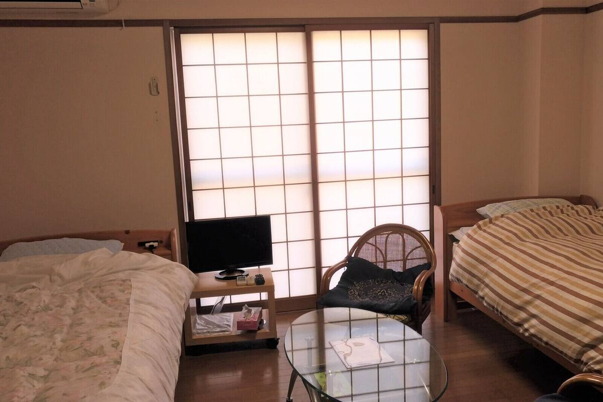 A room with two beds, a TV, a chair, and a small table.