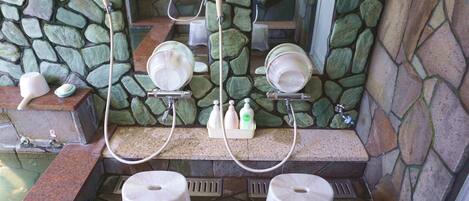 A bathroom with a stone wall, two sinks with faucets, and a mirror above the sinks.