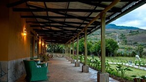 A covered outdoor area with a stone floor, green chairs, and a view of a garden and hills in the background. - Tambo Sapalanchan Lodge (Lámud)