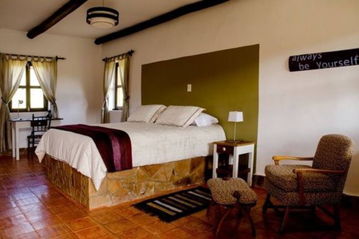 A bedroom with a bed, a chair, a desk, and a wall sign.