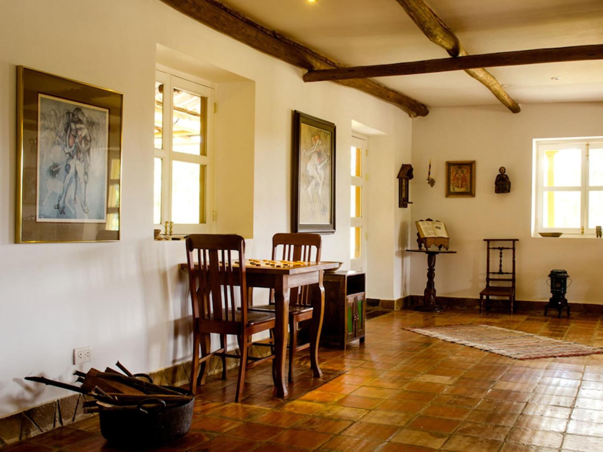 Un comedor con una mesa y sillas de madera, piso de baldosas y obras de arte en las paredes.