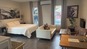 Una habitación de hotel con cama, sofá, mesa de comedor, televisión y ventilador de techo.