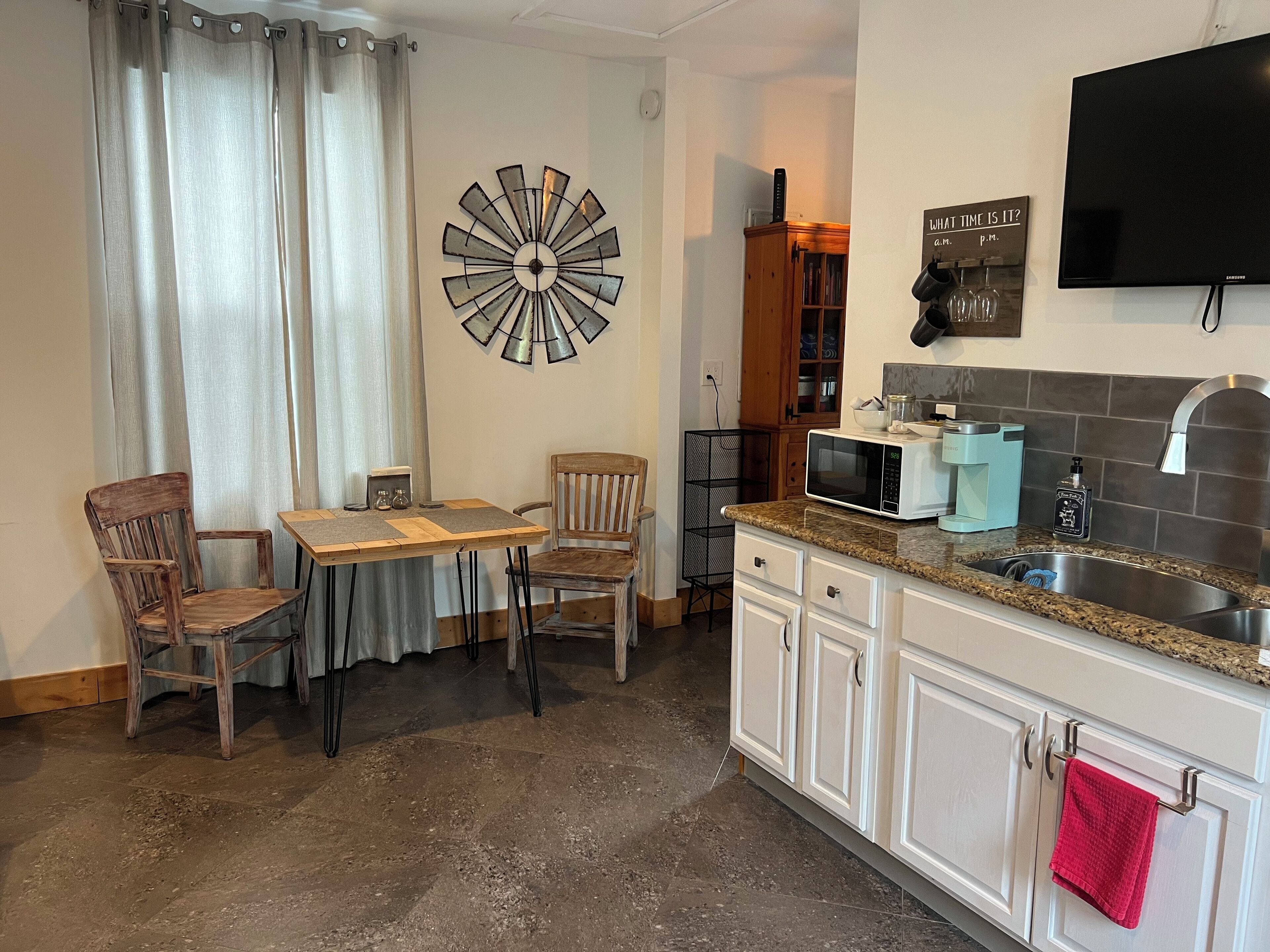 Une cuisine compacte comprenant une table à manger, des chaises, un four à micro-ondes, un évier et un téléviseur fixé au mur.
