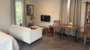 Una habitación con un sofá blanco, una mesa de comedor de madera, un televisor y un ventilador de techo.