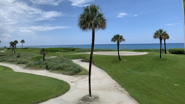 Un campo de golf con búnkeres de arena, palmeras y vista despejada al océano.