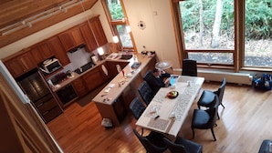 Una cocina moderna con armarios de madera, un comedor con mesa y sillas, y ventanas grandes que ofrecen vistas al exterior.
