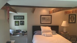 A bedroom with a bed, a nightstand, a lamp, framed pictures on the wall, and a window with curtains. - Great location for college visits/move-in, parents weekend, Merion Golf, Phila! (Ardmore)