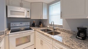 Una cocina con armarios blancos, microondas integrado, estufa, fregadero y cafetera.