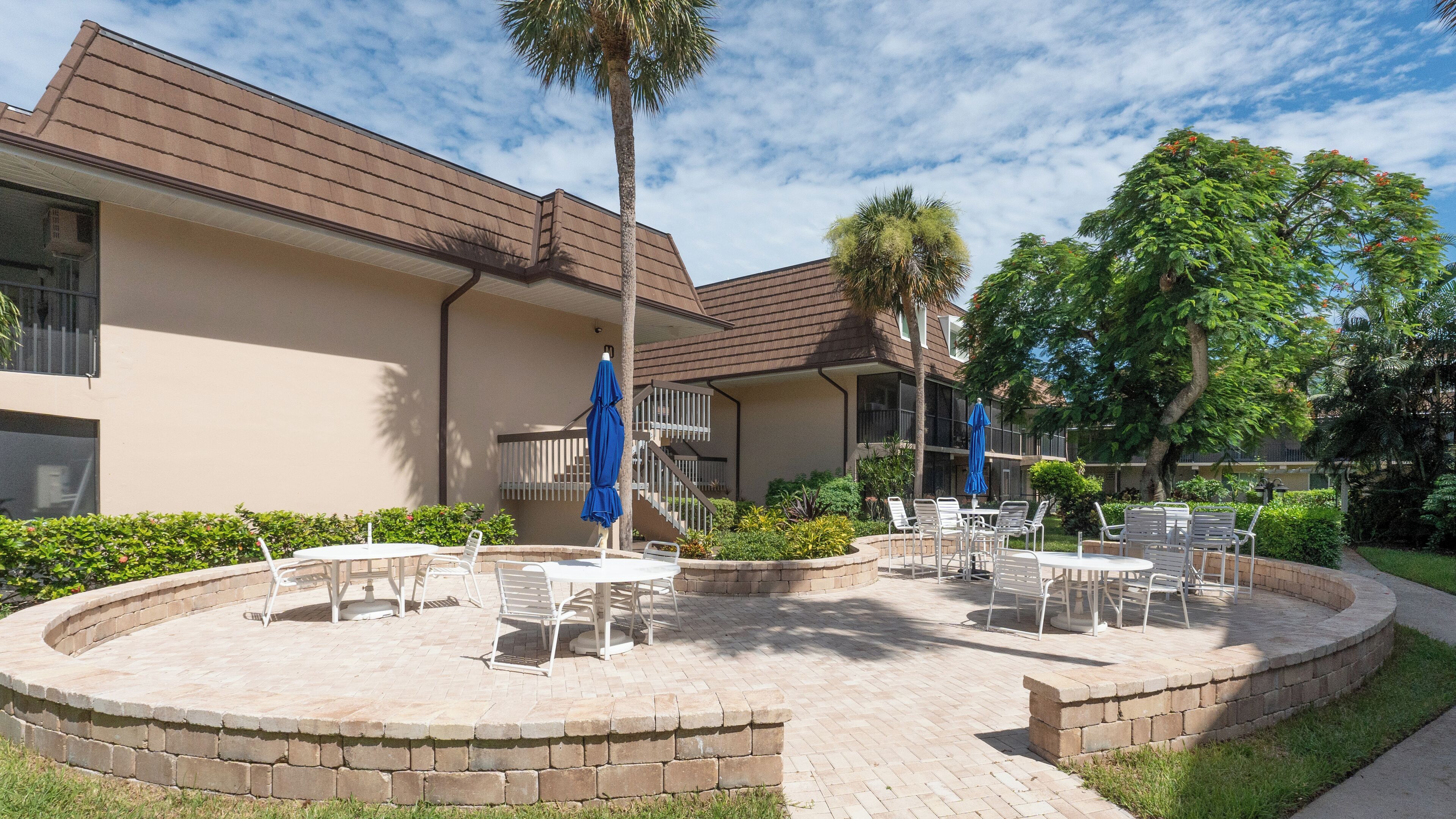 A courtyard with outdoor seating, a palm tree, and a building with a brown roof.