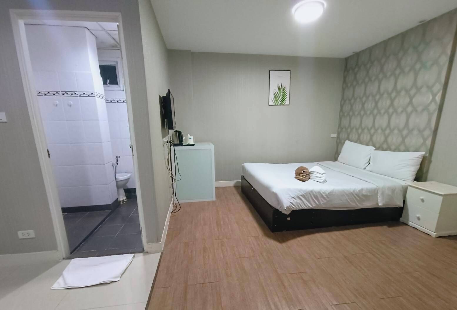 Un dormitorio con cama, mesitas de noche, un armario pequeño y un baño visible a través de una puerta abierta.