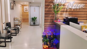 A reception area with a wooden wall, a reception desk, a potted plant, and a decorative altar with flowers and fruits.