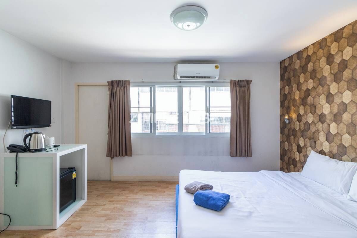 A hotel room with a bed, a desk with a television, and an air conditioning unit.