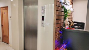 A modern elevator with a digital display, a no smoking sign, and a reception desk with a decorative plant and a small statue.