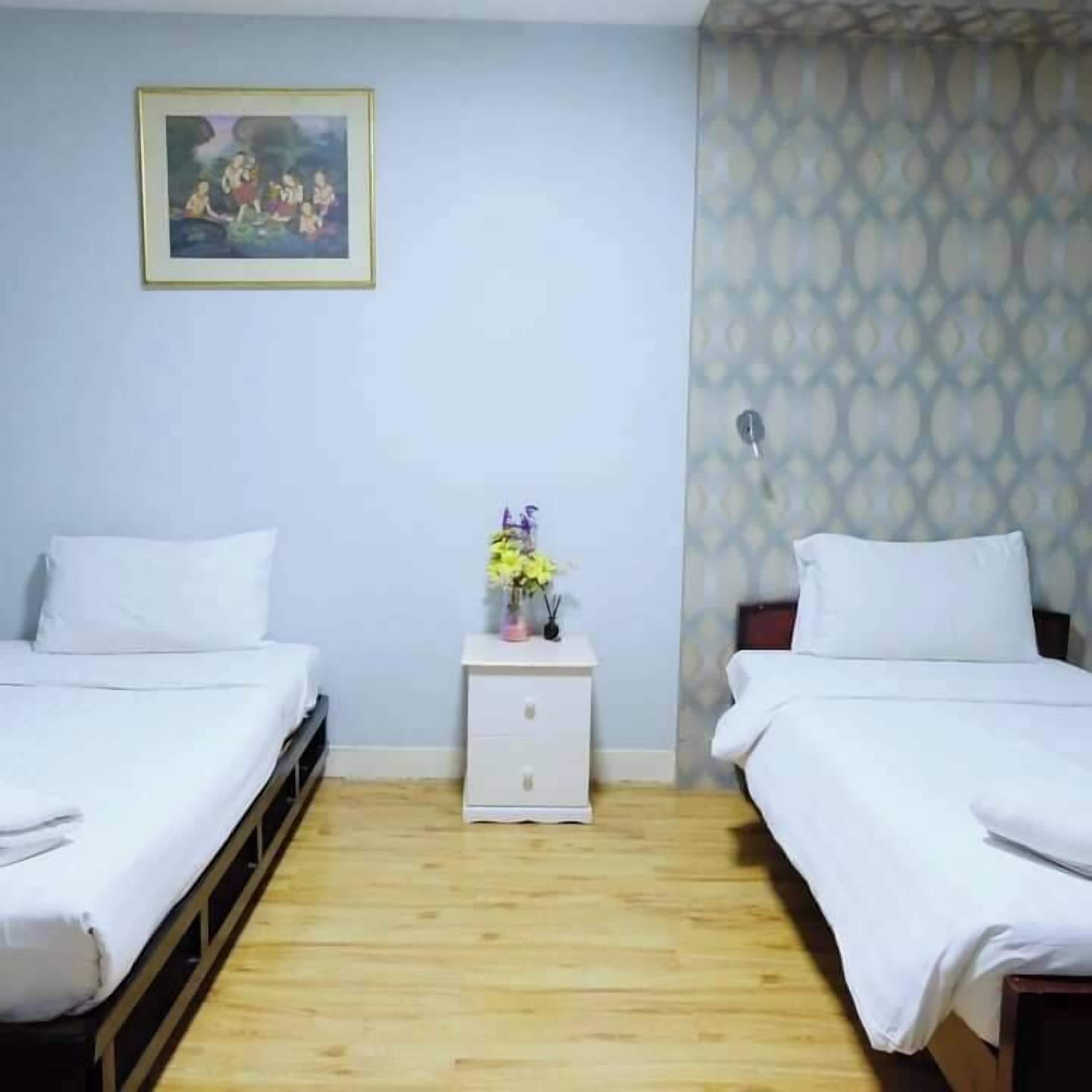 A room with two beds, a nightstand with a vase of flowers, and a patterned wallpaper.